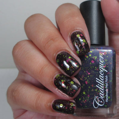 Thermal glitter and flake Cadillacquer nail polish in Strange Happenings, shown on eight squoval nails held alongside the bottle, nails display the cold state as near-black blackened eggplant loaded with matte neon chartreuse-green hex and dot glitter and hot pink iridescent flakes, bottle face shows the deeper blue-violet warm state, light skin tone, studio lighting, swatched by @_always_polished_