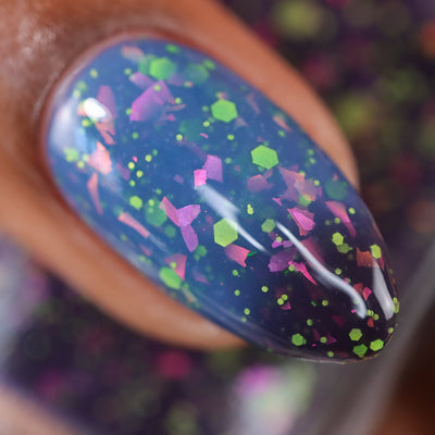 Thermal glitter and iridescent flake Cadillacquer nail polish in Strange Happenings, macro swatch on a single oval nail showing deep blackened navy-eggplant cold state transitioning to dusty blue warm state, packed with neon yellow-green matte hexagon and micro glitter and large pink-to-purple iridescent flakes, medium-deep skin tone, studio lighting, swatched by @doseoflolade