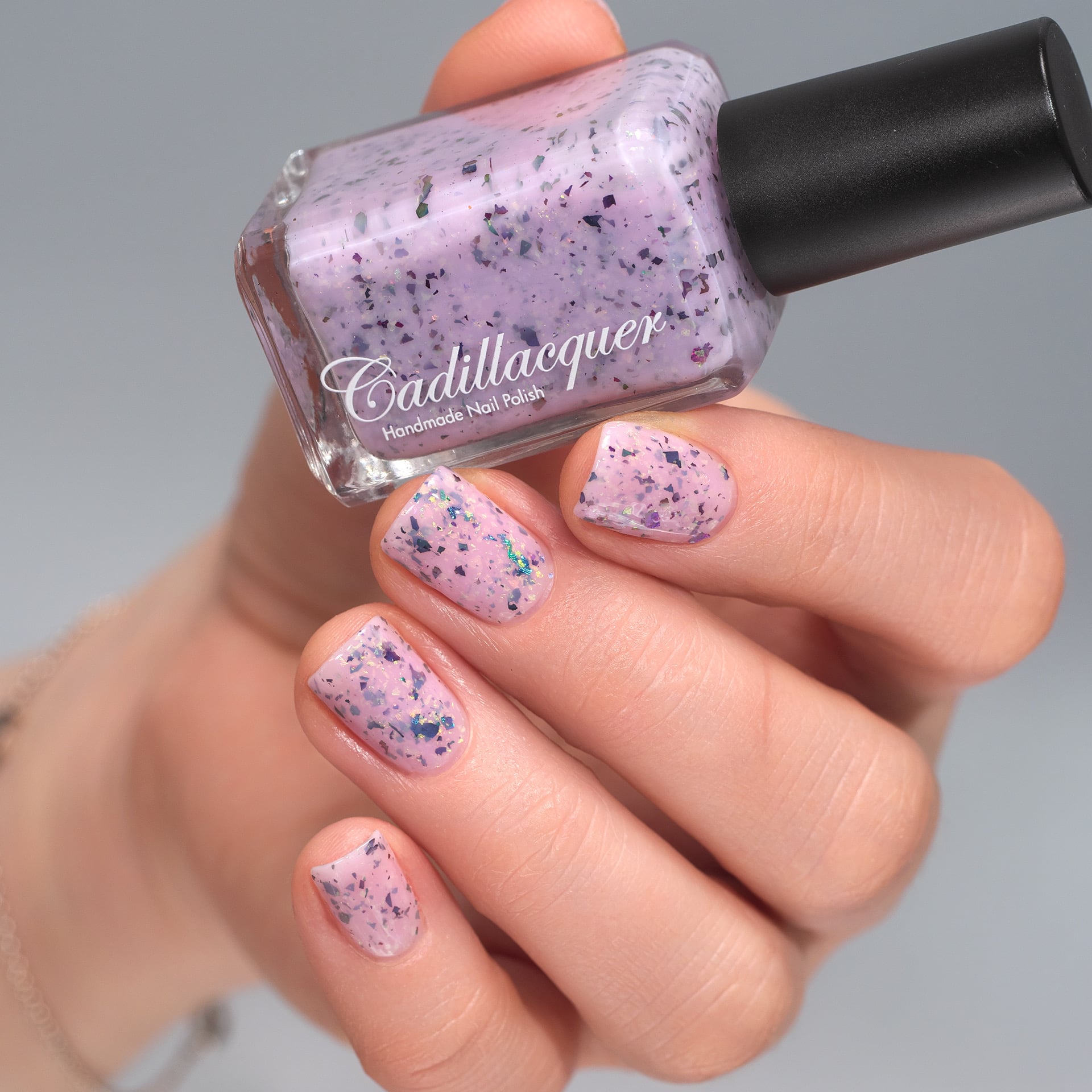 Cadillacquer Sweet Nothing pink teal chameleon iridescent crelly nail polish, bottle held with four-nail swatch, light skin, studio lighting