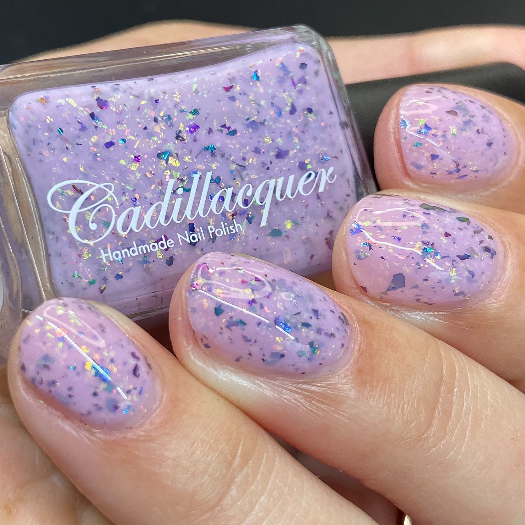 Cadillacquer Sweet Nothing pink teal chameleon iridescent crelly nail polish, bottle held with four-nail swatch, light skin, studio lighting