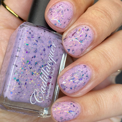 Cadillacquer Sweet Nothing pink teal chameleon iridescent crelly nail polish, bottle held with four-nail swatch, light skin, studio lighting