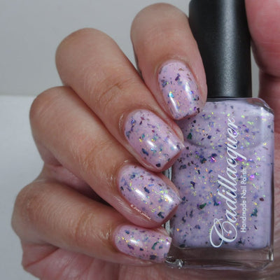 Cadillacquer Sweet Nothing pink teal chameleon iridescent crelly nail polish, bottle held with four-nail swatch, light skin, studio lighting