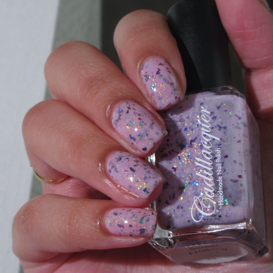 Cadillacquer Sweet Nothing pink teal chameleon iridescent crelly nail polish, bottle held with five-nail swatch, light skin, indoor warm lighting