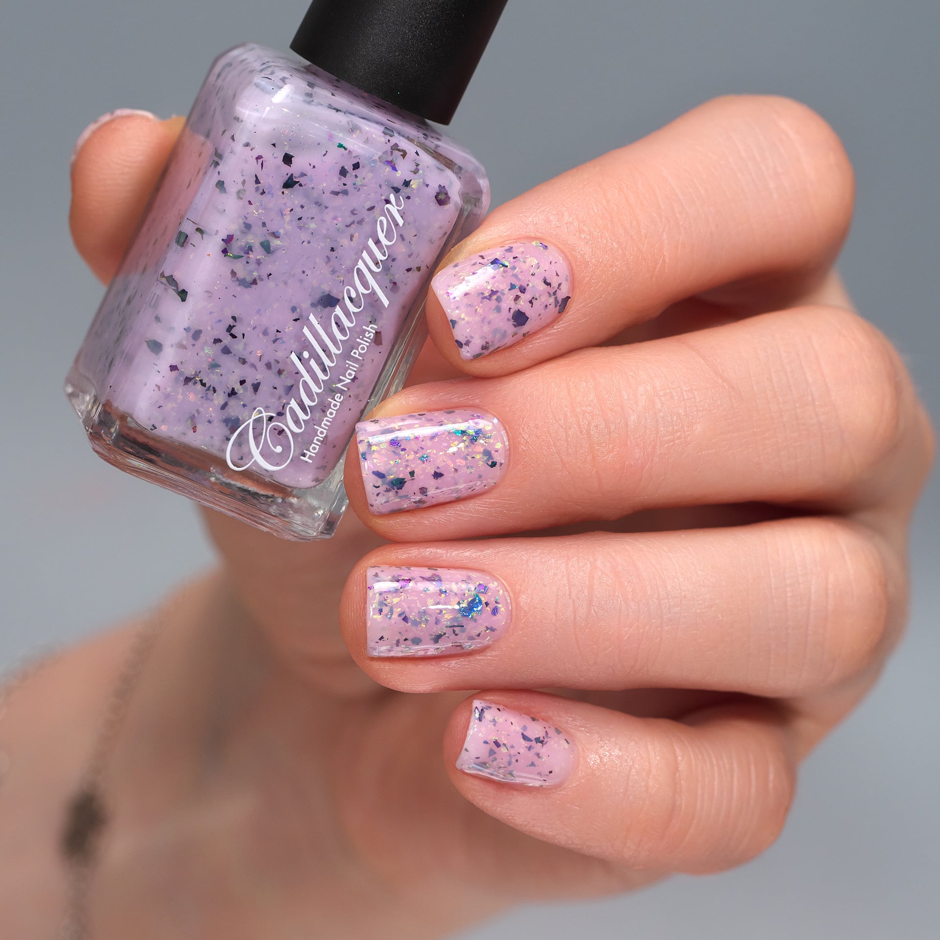 Cadillacquer Sweet Nothing pink teal chameleon iridescent crelly nail polish, bottle held with four-nail swatch, light skin, studio lighting
