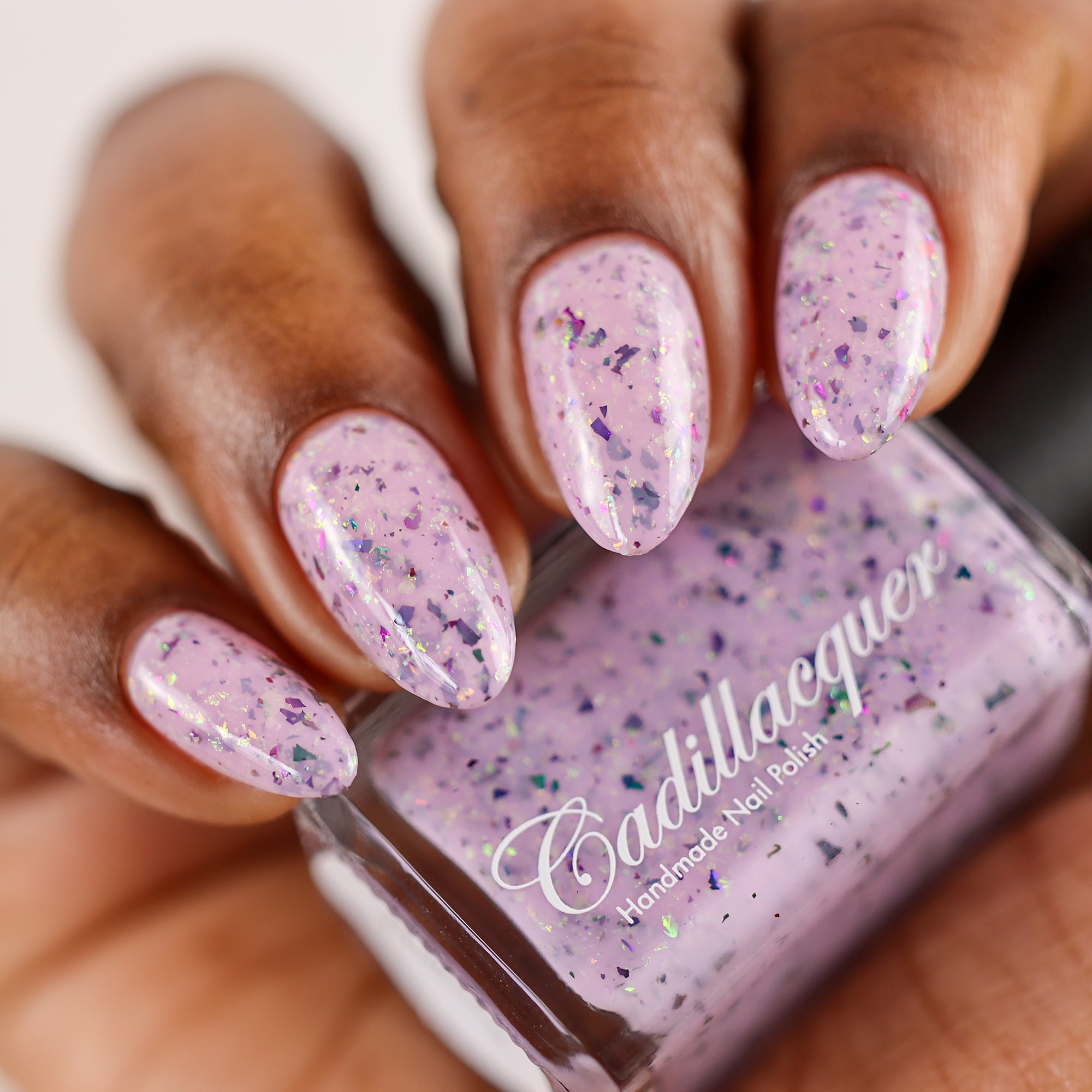 Cadillacquer Sweet Nothing pink teal chameleon iridescent crelly nail polish, bottle held with four-nail swatch, deep skin, studio lighting