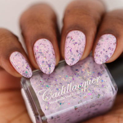Cadillacquer Sweet Nothing pink teal chameleon iridescent crelly nail polish, bottle held with four-nail swatch, deep skin, studio lighting