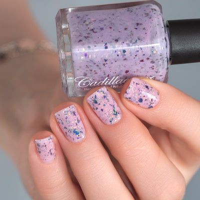 Cadillacquer Sweet Nothing pink teal chameleon iridescent crelly nail polish, bottle held with four-nail swatch, light skin, studio lighting