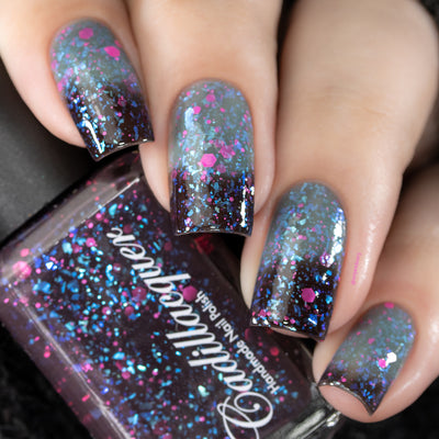Thermal glitter-and-flake Cadillacquer nail polish in What Lurks Within, shown as a bottle-and-nails swatch on five square nails, displaying a dramatic thermal transition from blackened eggplant at the nail base to muted blue-grey at the tips, loaded with matte neon magenta-pink glitter in multiple sizes and cyan-blue iridescent flakes throughout, light skin tone, studio lighting, swatched by @serpentine13