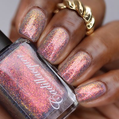 Iridescent multichrome micro-flake and reflective glitter Cadillacquer nail polish in You Wished For This, shown swatched on five short natural nails with a sheer mauve-grey base packed with warm orange-to-pinkish-red-to-golden-yellow iridescent micro flakes and scattered charcoal and blue holographic micro-glitter, on deep skin tone with a gold ring accent, studio lighting, swatched by @lacquer_is_life