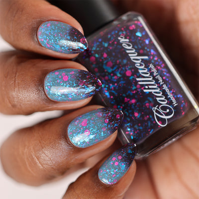 Thermal glitter-and-flake Cadillacquer nail polish in What Lurks Within, swatched on deep skin tone almond nails showing a blackened eggplant cold state at the tips transitioning to blue-grey warm state at the nail bases, packed with iridescent cyan-blue flakes and matte neon pink glitter in mixed hex and dot sizes, with the matching bottle visible, shot under studio lighting, swatched by @doseoflolade