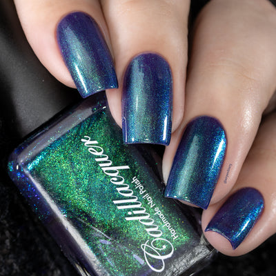 Multichrome holographic shimmer Cadillacquer nail polish in What Could Possibly Go Wrong?, swatched on four square nails alongside the bottle, shifting from deep indigo-violet through royal blue to vivid teal-green depending on angle, bottle face dominated by brilliant green shimmer flash, light skin tone, studio lighting, swatched by @serpentine13