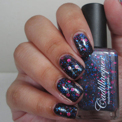 Thermal glitter and flake Cadillacquer nail polish in What Lurks Within, shown swatched on four fingers of one hand alongside the bottle held in the other hand, displaying a deep blackened eggplant-black cold state base loaded with bright cyan-blue iridescent flakes and scattered neon hot pink matte glitter hexes of varying sizes, light skin tone, indoor warm lighting, swatched by @_always_polished_