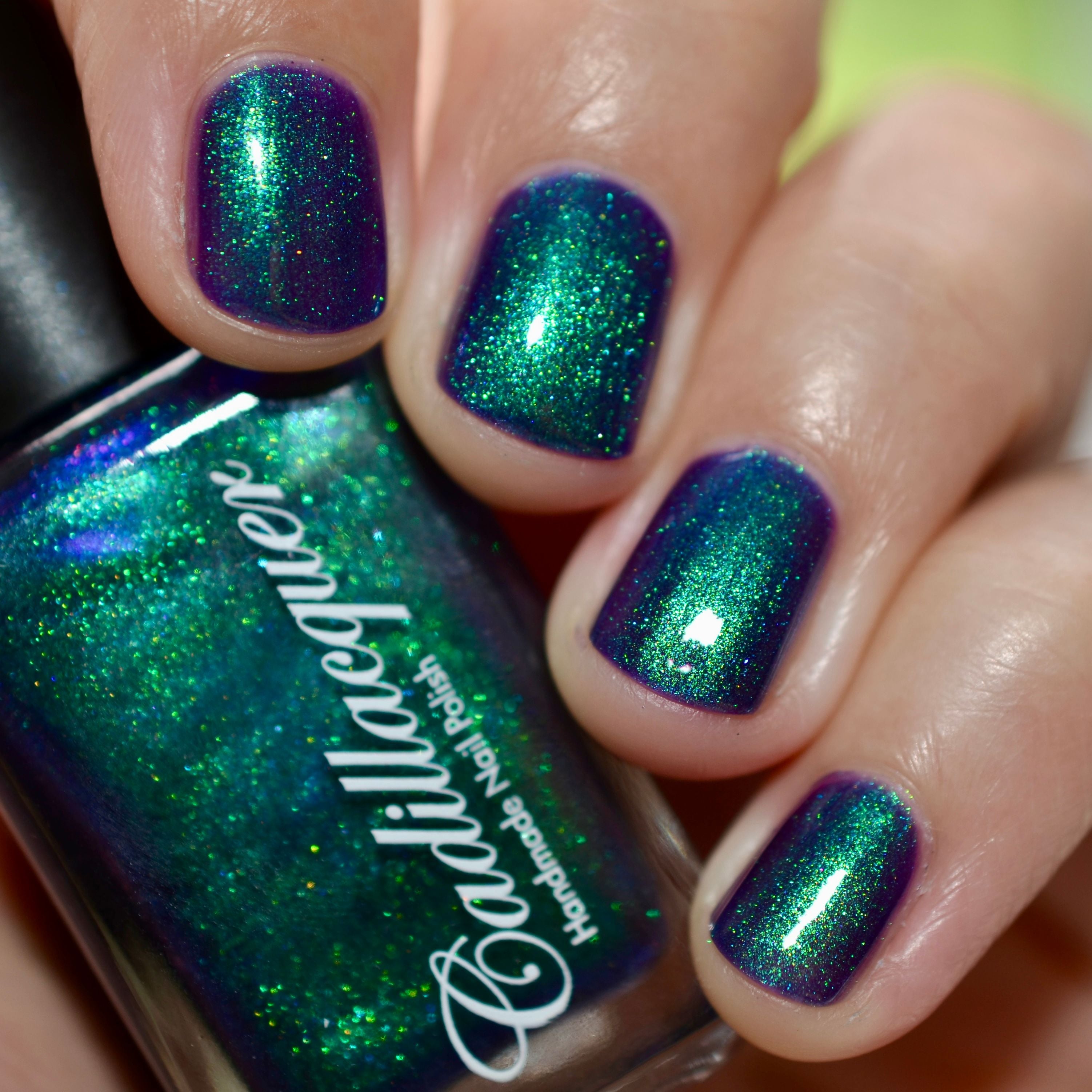 Multichrome shimmer Cadillacquer nail polish in What Could Possibly Go Wrong?, bottle held in hand alongside four swatched nails shifting from deep indigo-violet to vivid emerald green with bright lime and cyan shimmer flash, light-medium skin tone, bright daylight lighting, swatched by @caitlinswatches