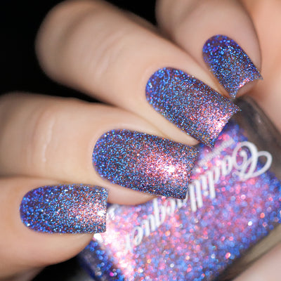 Multichrome glitter and micro-flake Cadillacquer nail polish in You Wished For This, shown on four oval nails with a blue-violet base shifting through pink-rose and copper-orange with scattered bright blue and charcoal reflective glitter particles, light-medium skin tone, direct flash lighting, swatched by @yyulia_m
