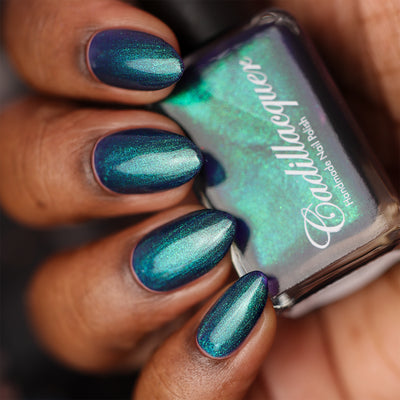 Multichrome shimmer Cadillacquer nail polish in What Could Possibly Go Wrong?, swatched on eight oval nails held alongside the bottle, shifting from deep indigo through dark teal to bright aqua-green depending on angle, deep skin tone, studio lighting, swatched by @doseoflolade