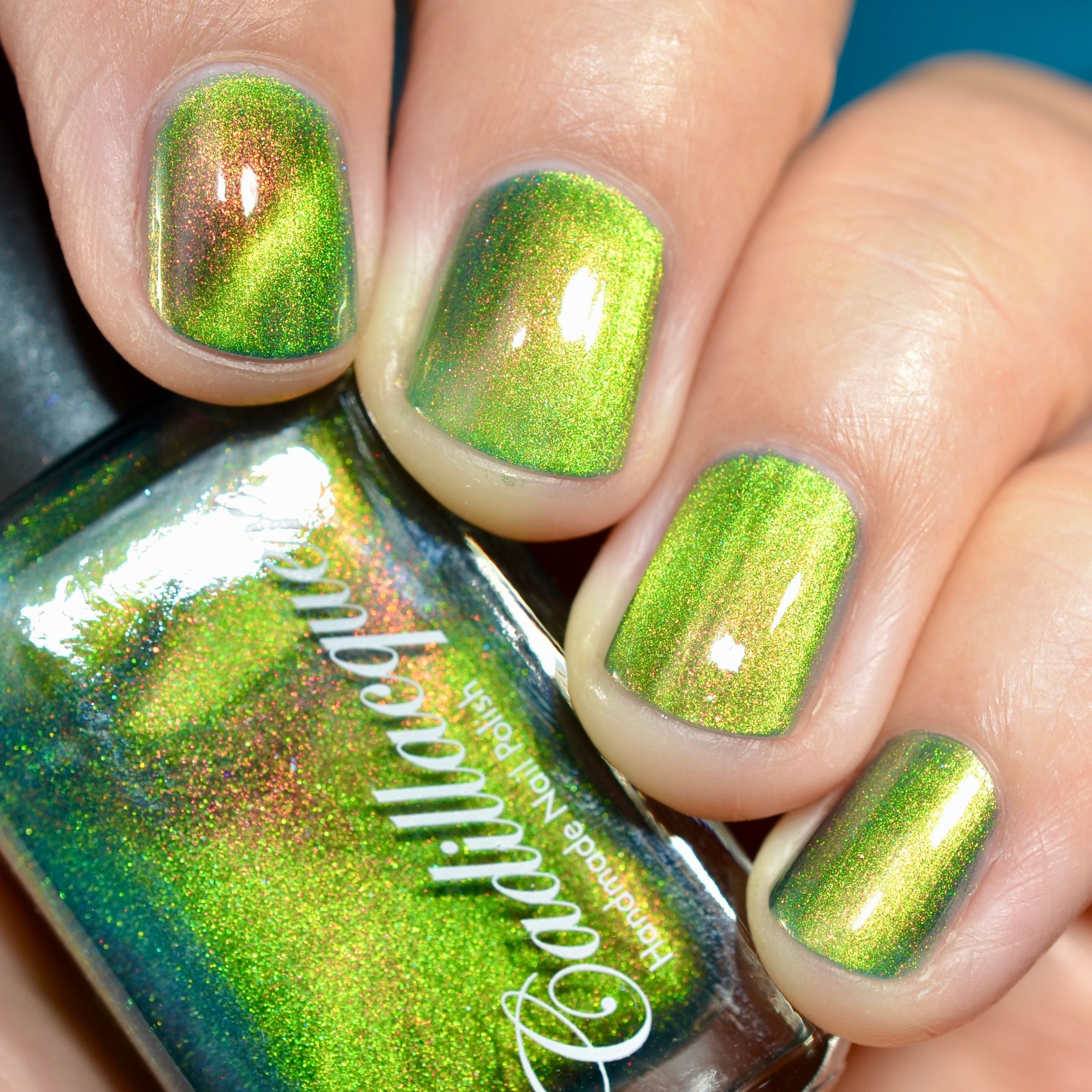 Holographic magnetic multichrome Cadillacquer nail polish in I Found A Place, swatched on five short natural nails showing a bright lime-green base with a warm copper-amber magnetic band and red-to-orange aurora shimmer flash, held alongside the polish bottle, light skin tone, direct flash lighting, swatched by @caitlinswatches