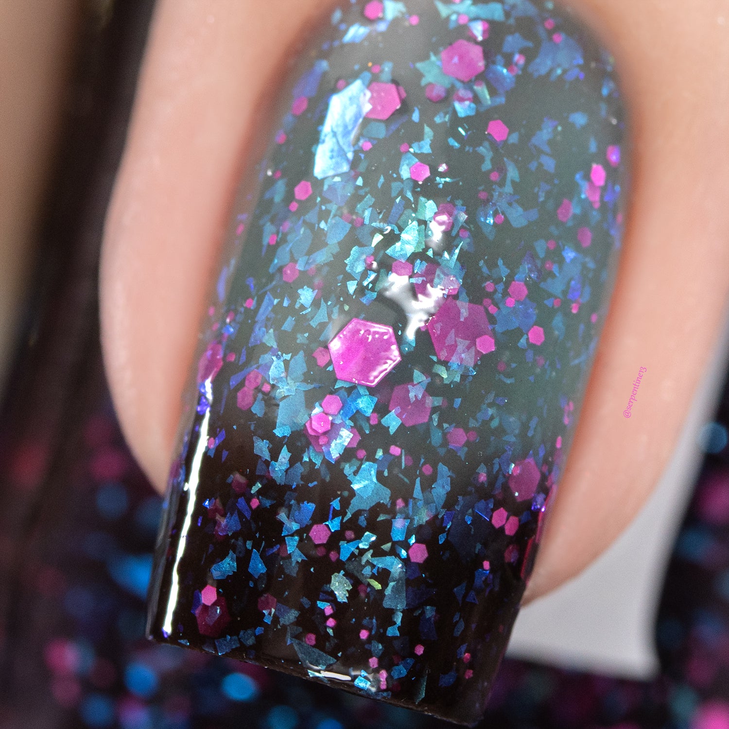 Thermal glitter and iridescent flake Cadillacquer nail polish in What Lurks Within, extreme macro swatch on a single oval nail showing blackened eggplant cold state at the tip transitioning to blueish grey warm state, densely packed with teal-to-blue iridescent medium flakes and scattered neon pink matte hexagon glitter in multiple sizes, light skin tone, studio lighting, swatched by @serpentine13