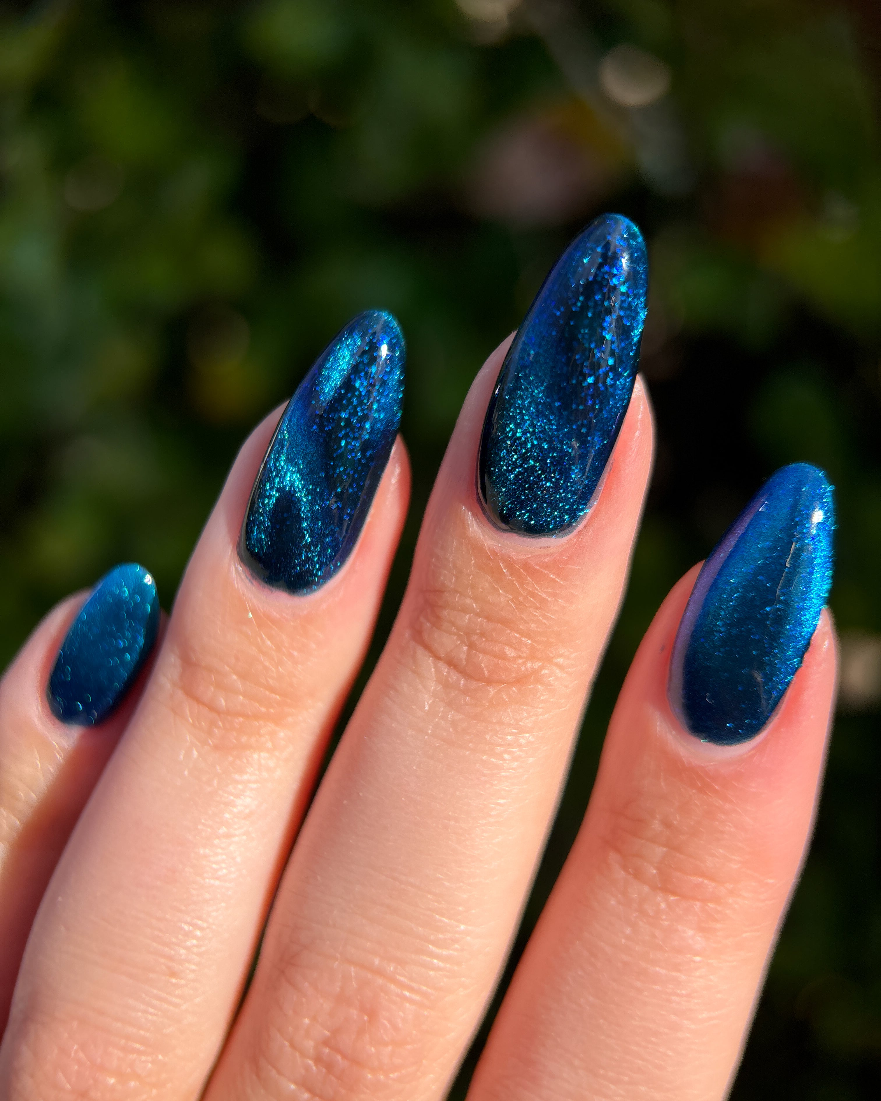 Heart of the Ocean by Glitch Lacquer on five long almond nails, deep blue magnetic jelly with bright magnetic stripe and blue glitters, light-medium skin tone, bright daylight.