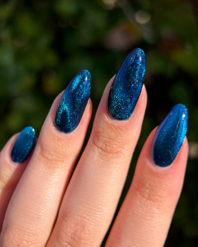 Heart of the Ocean by Glitch Lacquer on five long almond nails, deep blue magnetic jelly with bright magnetic stripe and blue glitters, light-medium skin tone, bright daylight.
