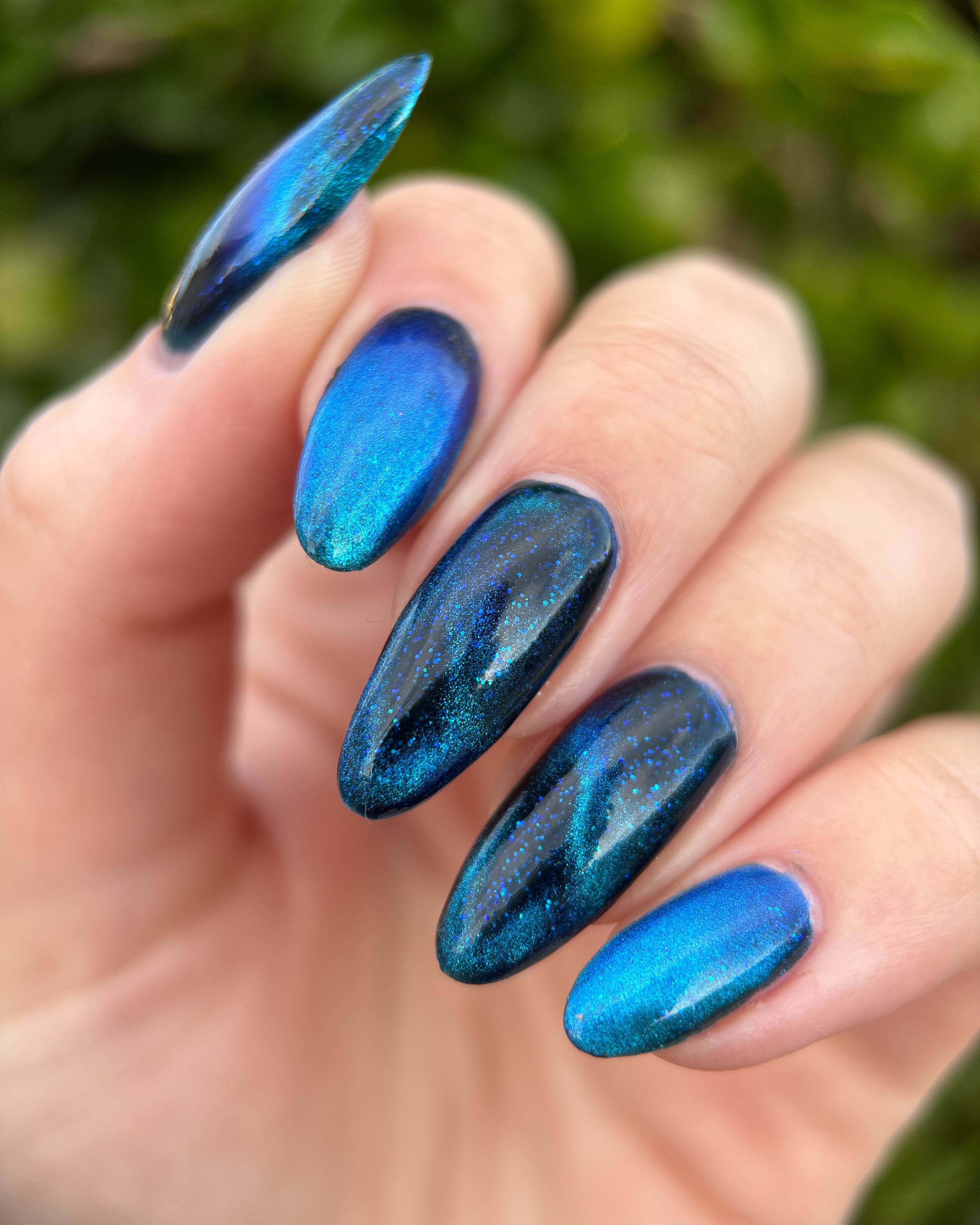 Heart of the Ocean by Glitch Lacquer on five long almond nails, deep blue magnetic jelly with blue glitters, light skin tone, bright daylight.