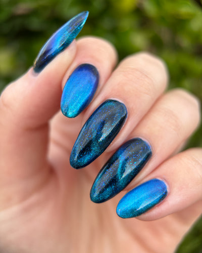Heart of the Ocean by Glitch Lacquer on five long almond nails, deep blue magnetic jelly with blue glitters, light skin tone, bright daylight.