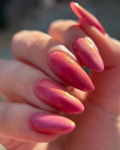 Lovey Dovey by Glitch Lacquer on five almond nails, warm pink polish with pink-to-gold reflective shimmer and silver magnetic pigment, light-medium skin tone, bright daylight.