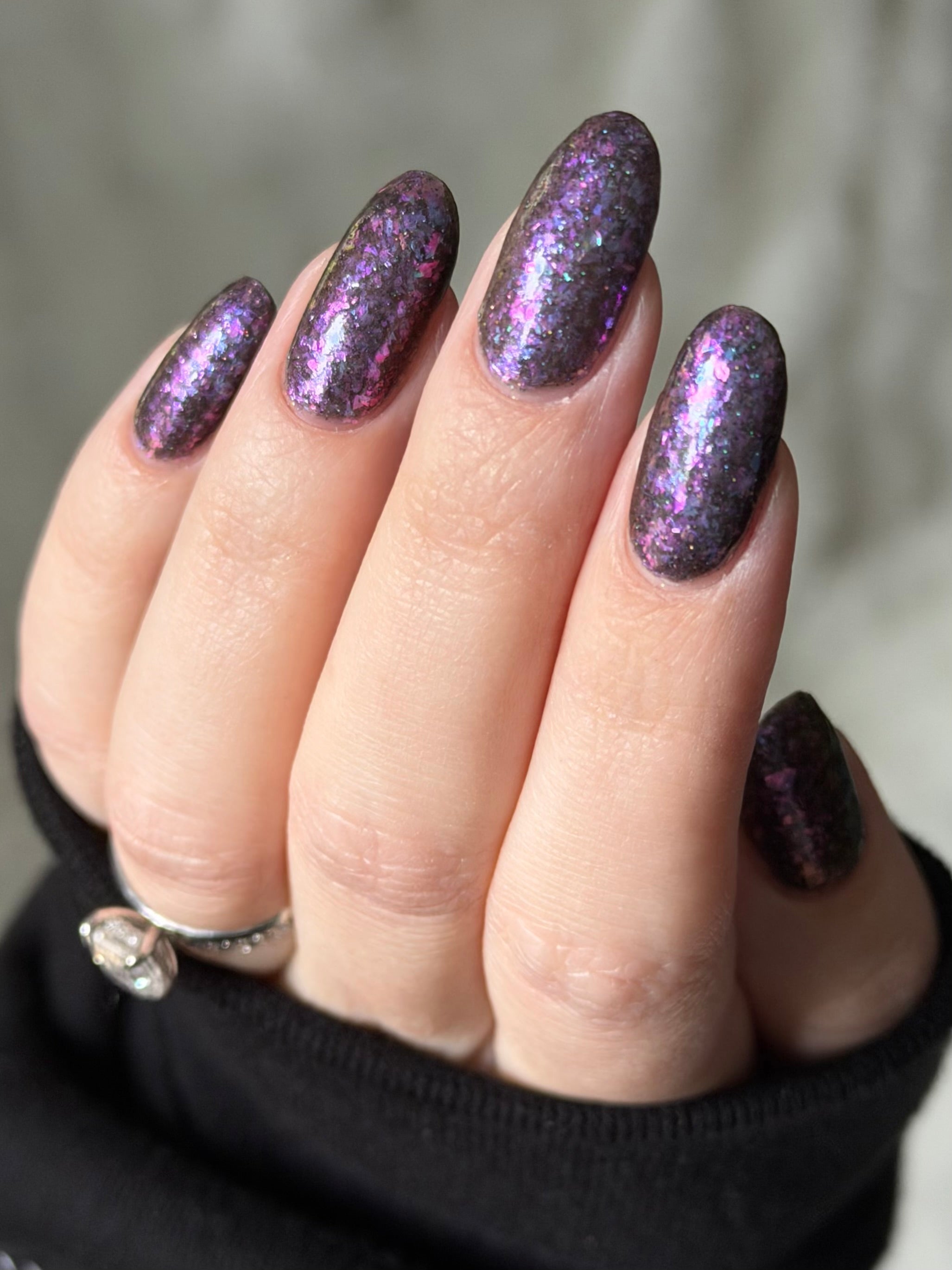 AVEN by Glitch Lacquer, soft black base, iridescent purple flakes, black holo micro-glitter, on light skin tone almond nails