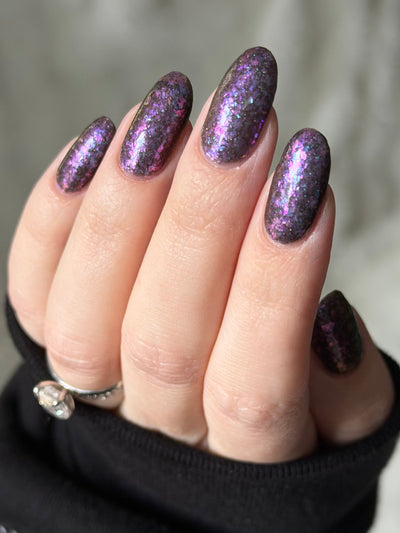 AVEN by Glitch Lacquer, soft black base, iridescent purple flakes, black holo micro-glitter, on light skin tone almond nails