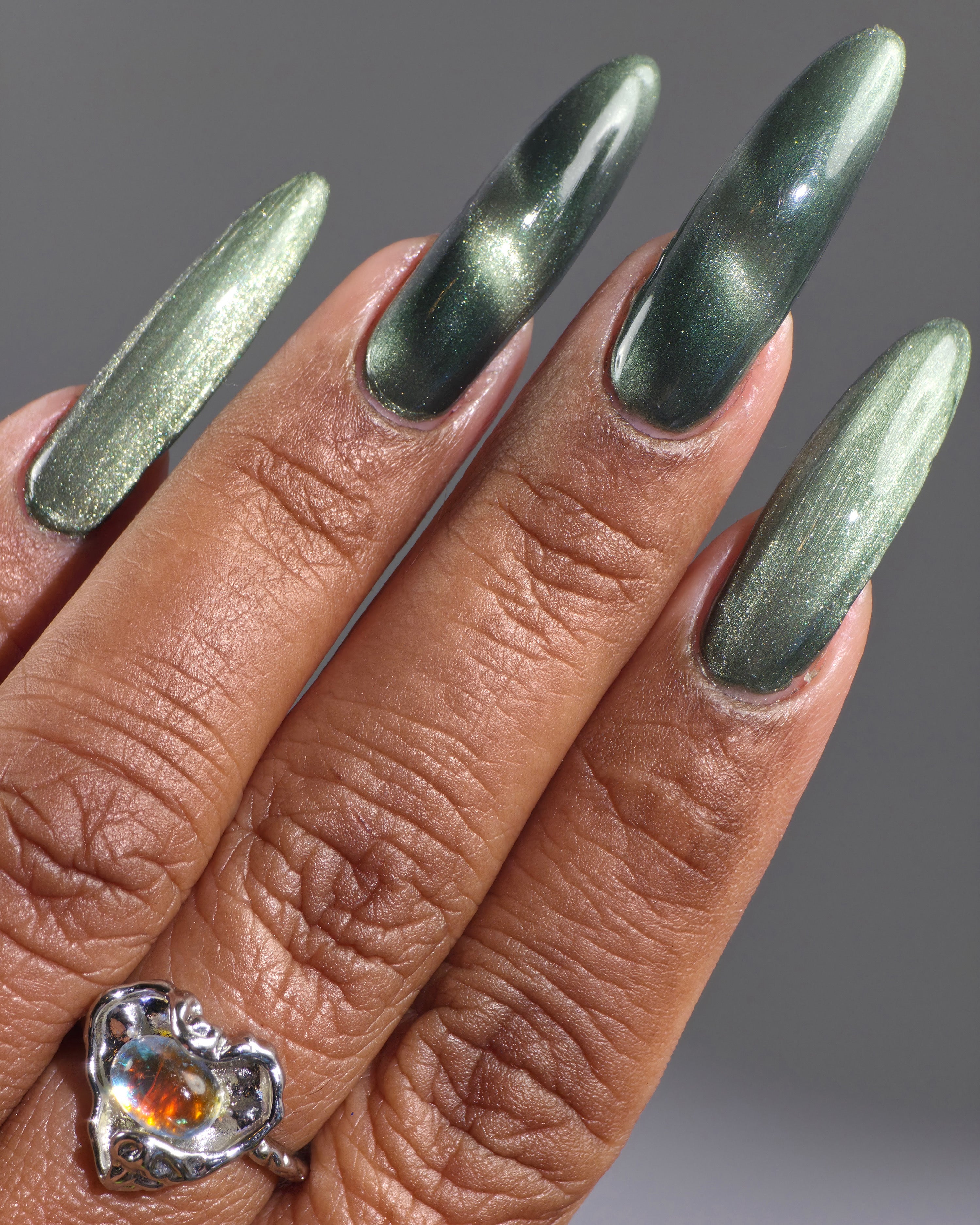 AUREA by Glitch Lacquer, blackened green base, greenish-gold magnetic cat-eye, on medium-deep skin tone almond nails