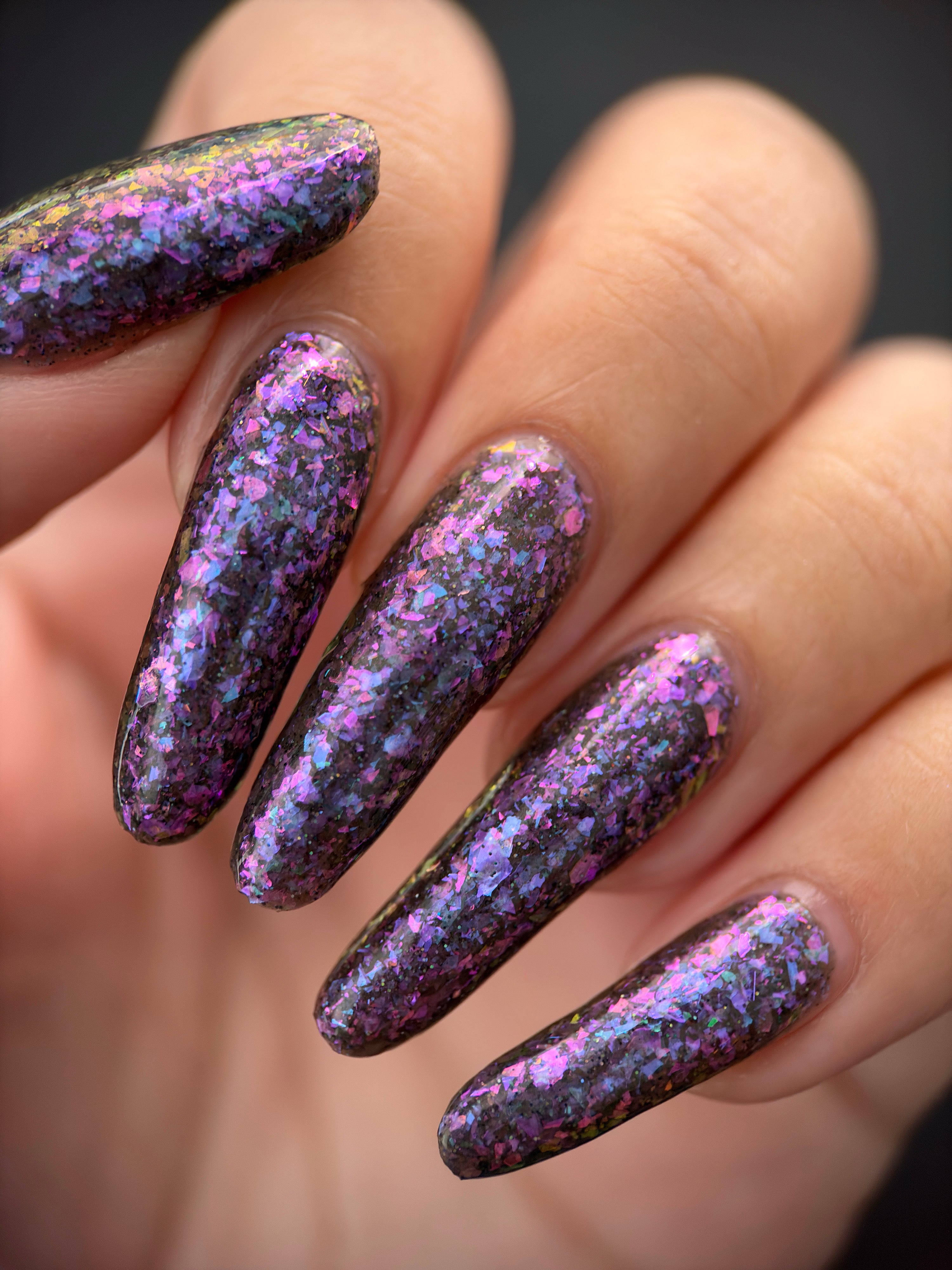 AVEN by Glitch Lacquer, soft black base, iridescent purple flakes, holo micro-glitter, on light-medium skin tone almond nails